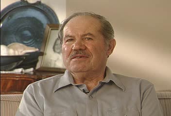 Sidney Iwens Survivor Testimony | author of How Dark the Heavens a Holocaust memoir from Lithuania to Latvia to Dachau with a headshot of the author in a casual grey shirt.